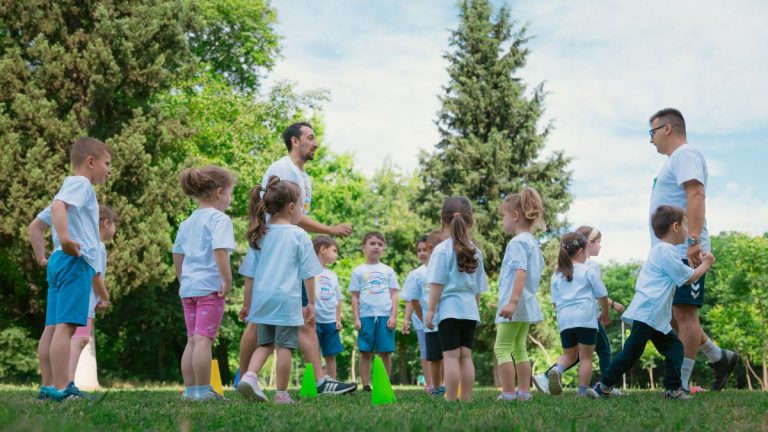 Group of children and teachers playing and learning in a sunny park setting.